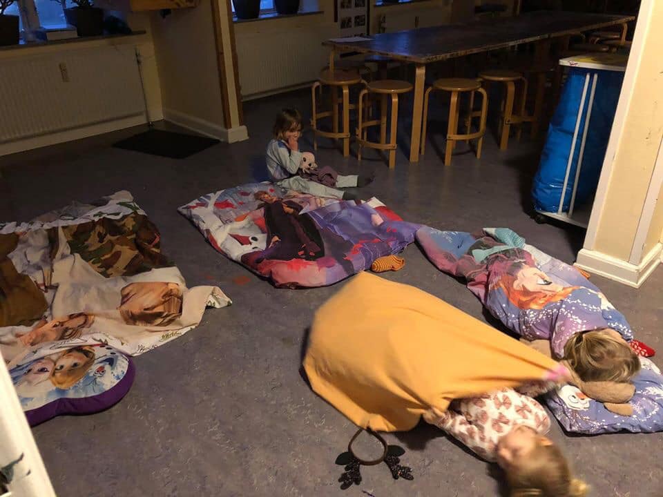 Børn ligger i nattøj og i deres dyner på gulvet i børnehaven