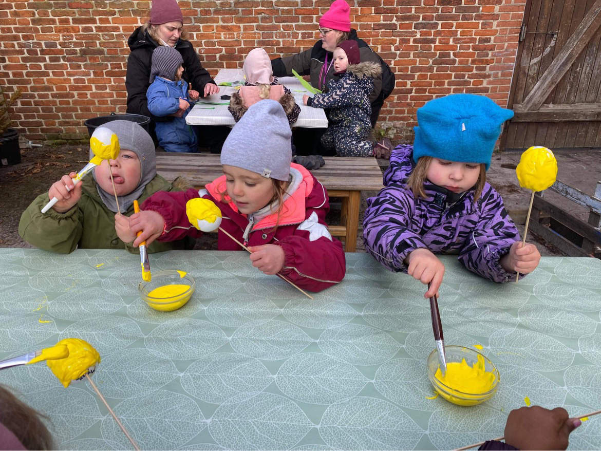 Børn sidder ved borde på legepladsen og maler flamingo æg, som bliver til flotte gule tulipaner
