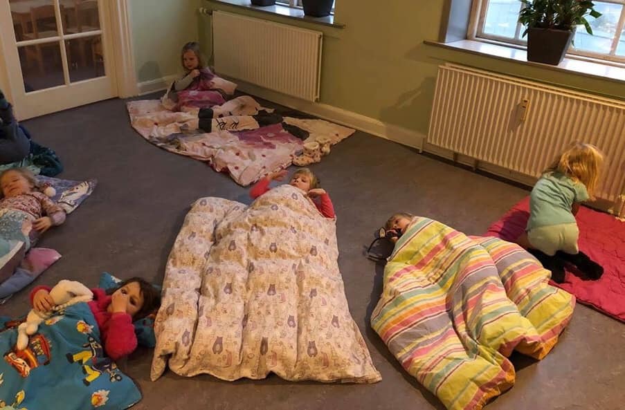 Børn ligger i deres nattøj i dyner på gulvet i børnehaven 