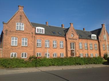 Billede af Børnehaven Taarnborg. Stort hus af røde mursten med mange vinduer.